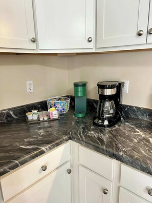 Eine Küche mit weißen Schränken, einer Marmorarbeitsplatte, einer Keurig-Kaffeemaschine, einer grünen Wasserflasche und einer Kaffeekanne.