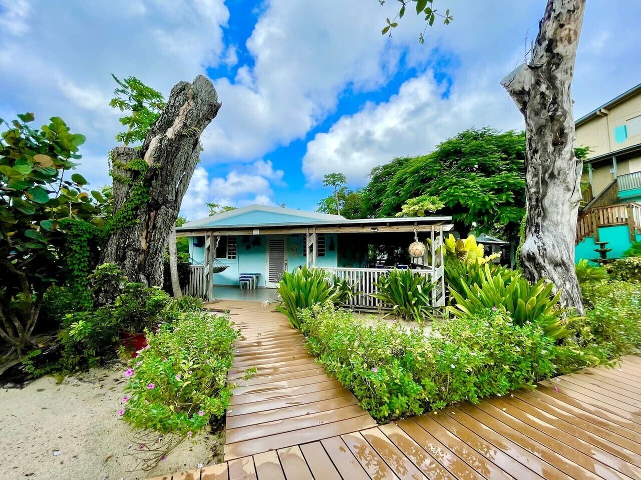 A beachfront property with a wooden deck, a covered porch, and lush greenery.
