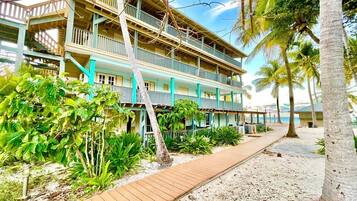A multi-story hotel with balconies, a wooden walkway, and tropical vegetation.