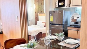 Een eetgedeelte met een glazen tafel, stoelen en een bed op de achtergrond.