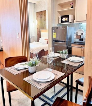Zona pranzo con tavolo in vetro, sedie e un letto sullo sfondo.