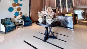 Een moderne lobby met een ronde tafel, blauwe fauteuils, decoratieve muurkunst en een houten receptiebalie.