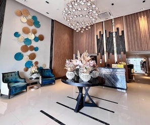 Una hall moderna con un tavolo rotondo, poltrone blu, opere d'arte decorativa e una reception in legno.