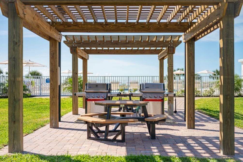 Un kiosque en bois équipé de deux barbecues et de tables de pique-nique.
