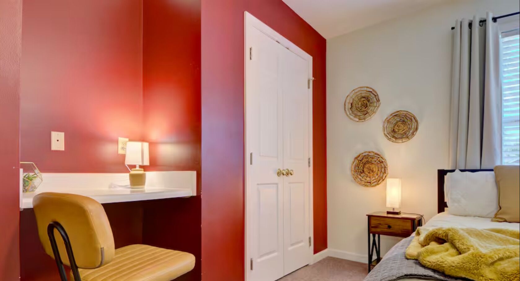 A room with a desk, chair, bed, bedside table, lamp, and wall decor.