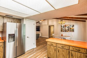 A kitchen with a refrigerator, water dispenser, wooden cabinets, and a dining area with a table and chairs. - Sunkissed Sassa|8PPL|FencedYard|1Dogok|Grill|ScreenedPorch (Homosassa)