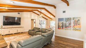 Una sala de estar con una televisión de pantalla plana grande, un sofá modular, vigas de madera y obras de arte en las paredes.