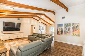 A living room with a large flat-screen TV, a sectional sofa, wooden beams, and artwork on the walls. - Sunkissed Sassa|8PPL|FencedYard|1Dogok|Grill|ScreenedPorch (Homosassa)