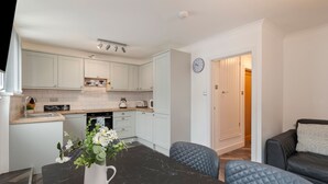 A modern kitchen with white cabinets, a black marble countertop, and a clock on the wall. - Smugglers Cove - Short Walk to Beach (Amroth)