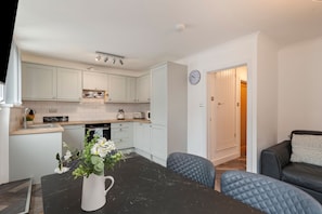 A modern kitchen with white cabinets, a black marble countertop, and a clock on the wall. - Smugglers Cove - Short Walk to Beach (Amroth)
