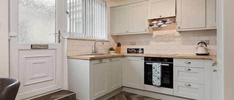 A kitchen with white cabinets, a herringbone wood floor, a built-in oven, and a window with blinds.