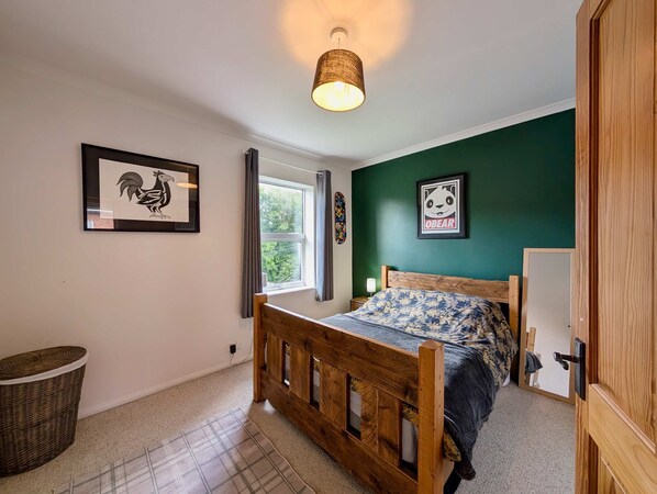 A bedroom with a wooden bed, a window with curtains, a wall-mounted lamp, and framed pictures. - Cosy 2bed house in Reading (Reading)