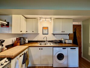 A compact kitchen with white cabinets, a built-in washing machine, a sink, and a stove. - Cosy 2bed house in Reading (Reading)