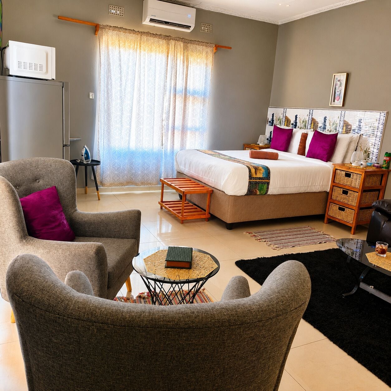 A modern bedroom with a bed, a seating area with a chair, a small table, and a bedside table with a lamp.