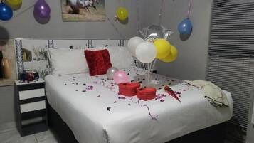 Un dormitorio con cama, almohadas, una mesita de noche y globos.