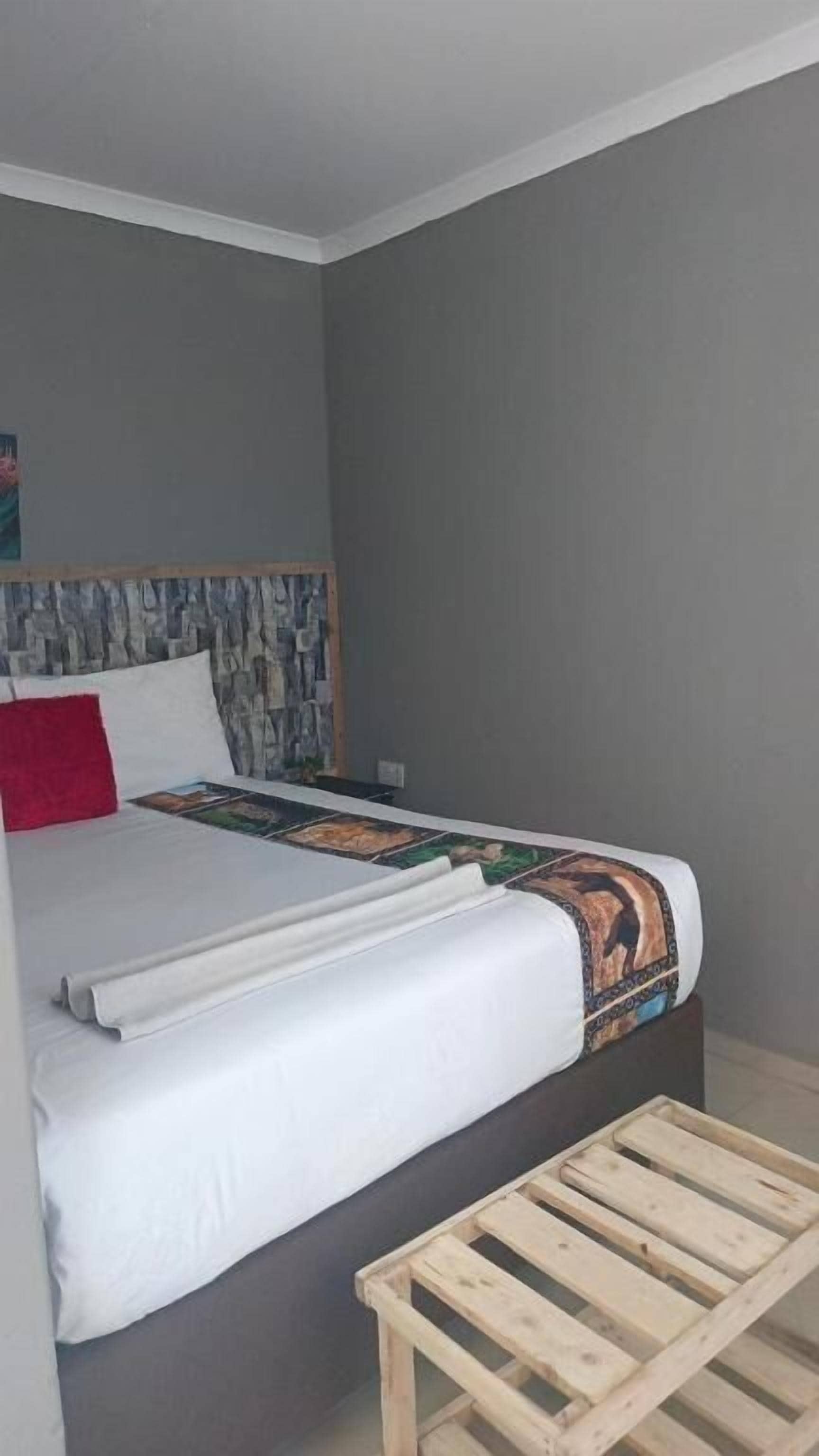 A bed with a headboard, a wooden bench, and a wall with a textured pattern.
