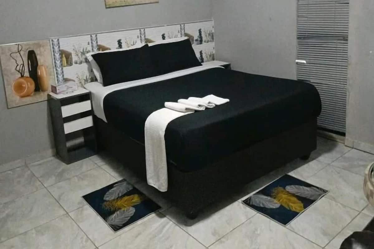 A bedroom with a bed, a nightstand, a wall-mounted air conditioner, and a window with blinds.