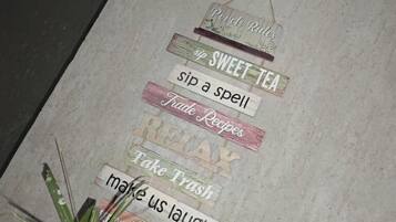 Una pared con varios letreros, incluyendo 'Sip Sweet Tea', 'Take Trash' y 'Make Us Laugh'.