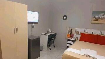 Um quarto com uma cama, uma escrivaninha, uma televisão e um guarda-roupa.