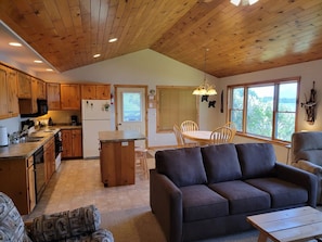 A cozy interior with wooden ceilings, a kitchen with wooden cabinets, a dining area with a table and chairs, and a sofa.