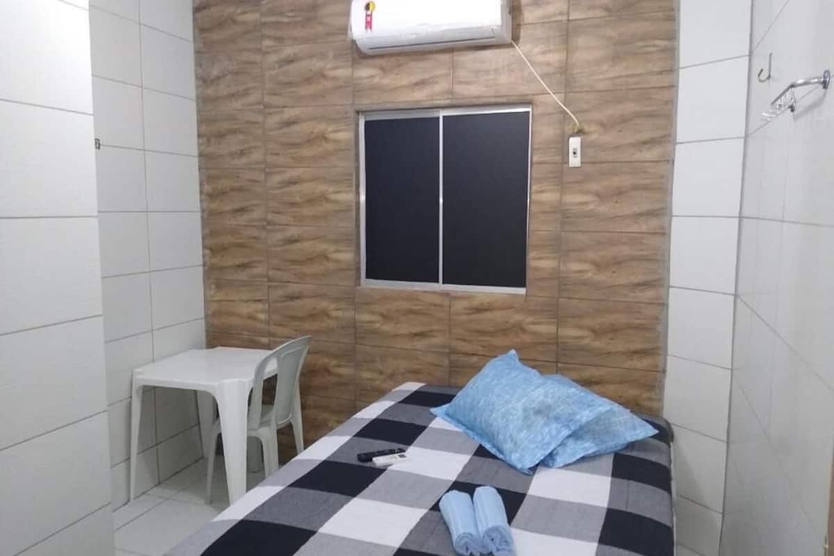 A room with a bed, a window, a chair, and an air conditioning unit.