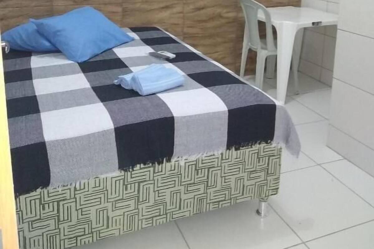 A bedroom with a bed, a window, a desk, and an air conditioner.