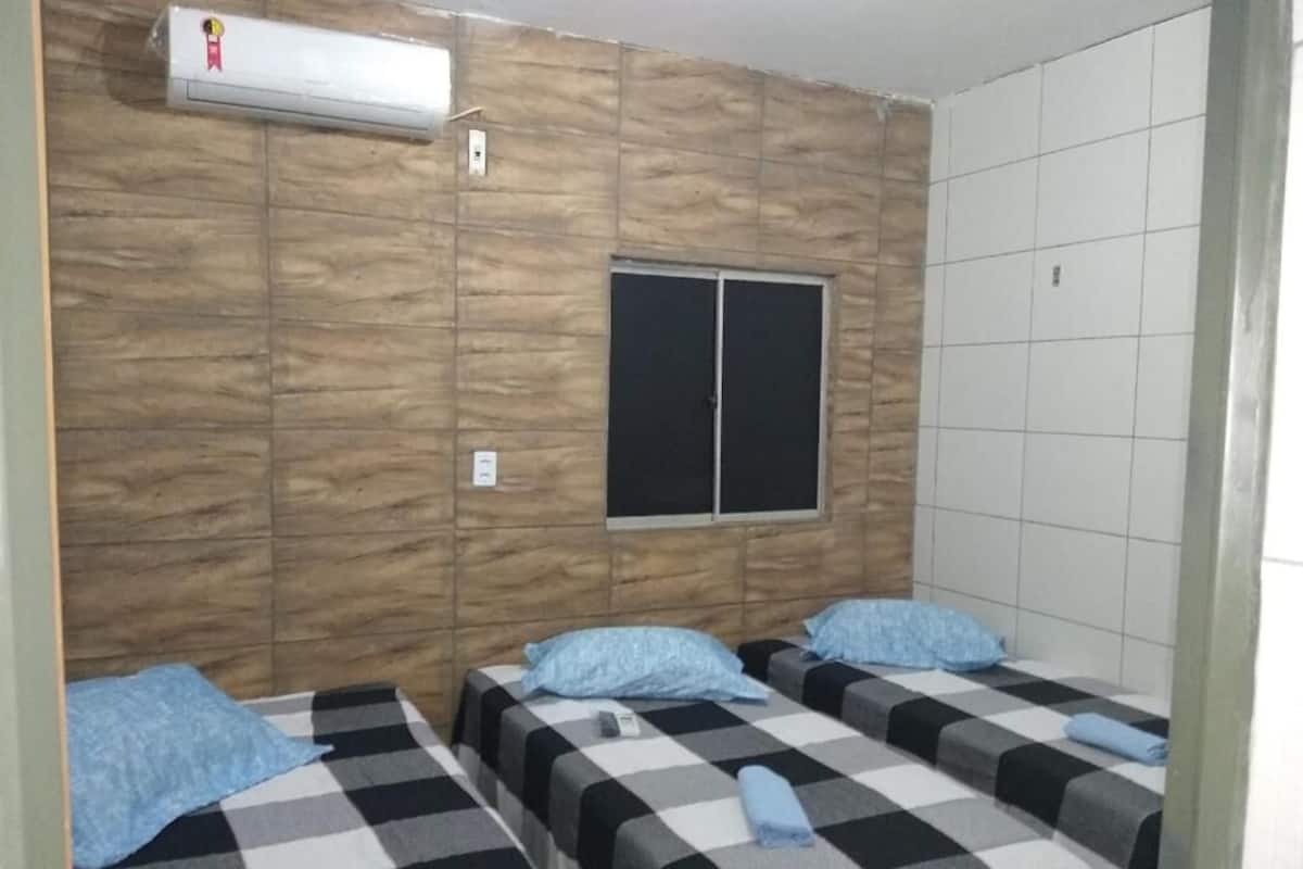 A room with three beds, a window, and a wall-mounted air conditioner.