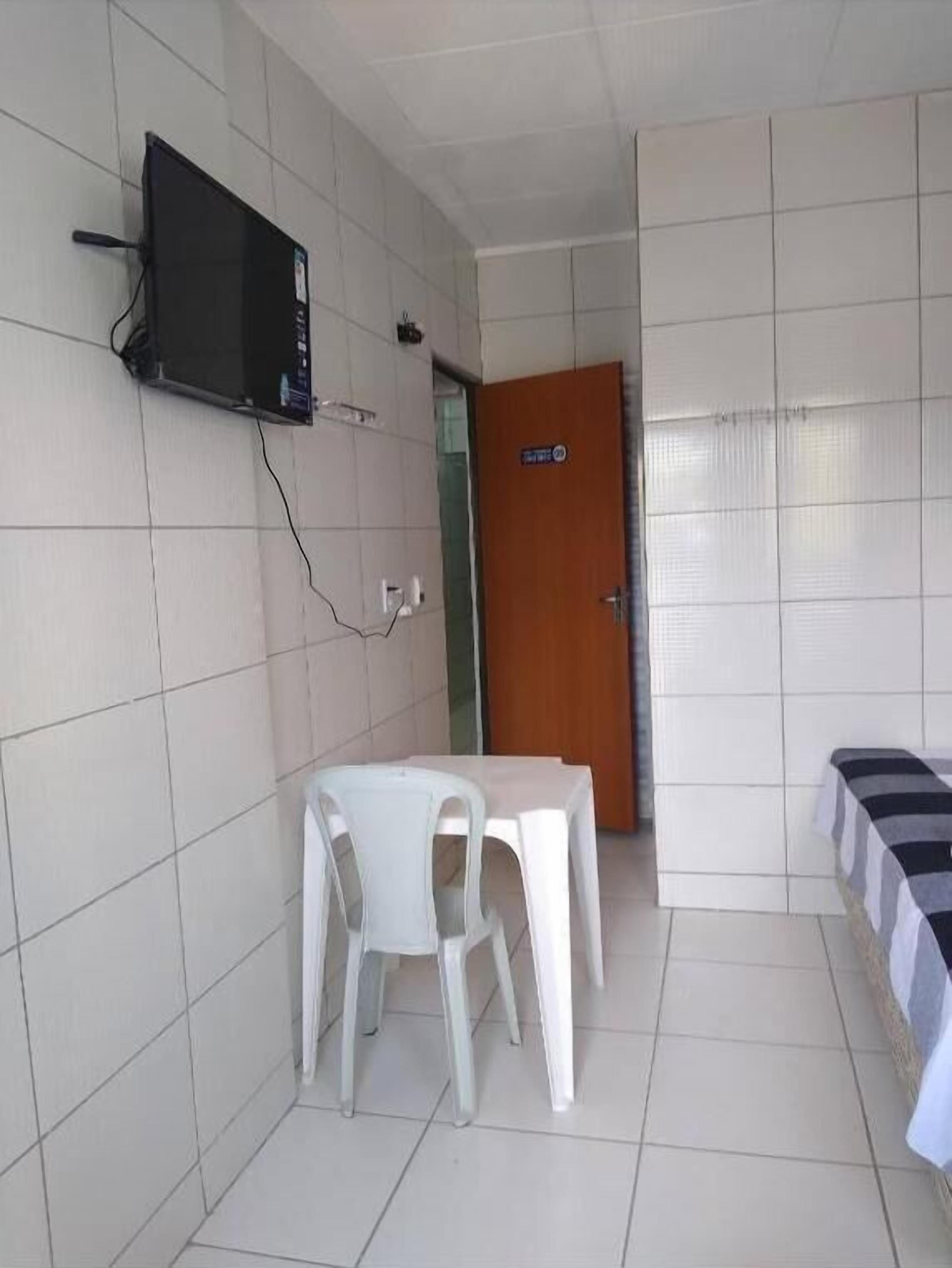 A room with a television mounted on the wall, a table with chairs, a door, and a bed with a striped bedspread.
