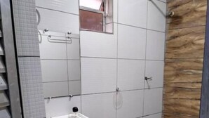 A bathroom with a tiled floor, a white sink, a mirror, a shower, and a wooden accent wall.