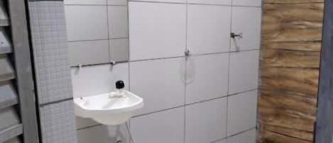 Un baño con piso de baldosas, un lavamanos blanco, un espejo, una ducha y una pared decorativa de madera.