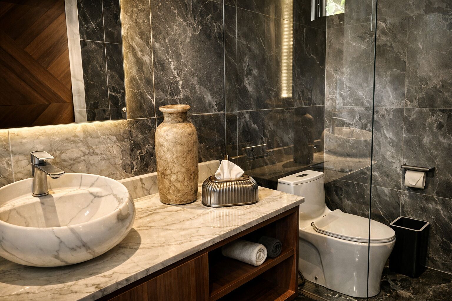 A bathroom with a marble sink, a large vase, a tissue dispenser, a toilet, and a trash bin.