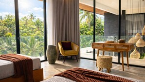 A modern bedroom with a large bed, a chair, a desk, and a view of lush greenery. - Oran Villa Bali (Tampaksiring)