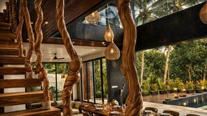 A modern dining area with a wooden staircase, hanging lights, and a view of the outdoors. - Oran Villa Bali (Tampaksiring)