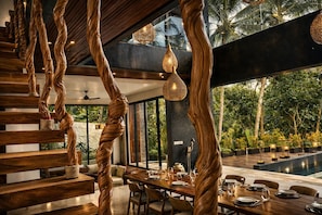 Un comedor moderno con una escalera de madera, luces colgantes y vistas al exterior.