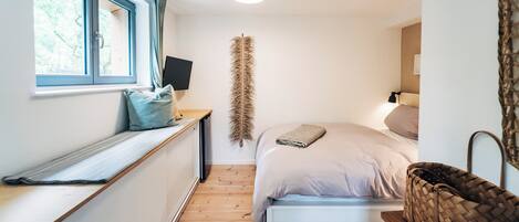 Un dormitorio con cama, ventana, escritorio, lámpara y cesta tejida.