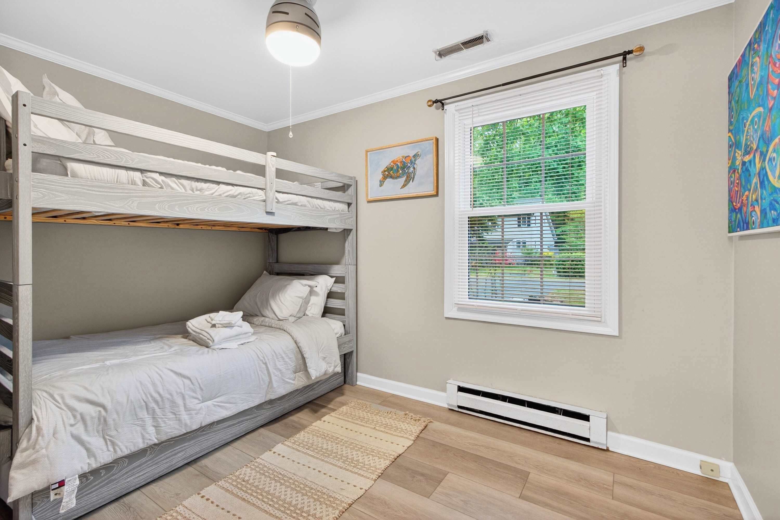 Une chambre avec un lit superposé, une fenêtre, un radiateur et un tableau encadré au mur.