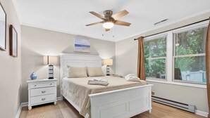 Un dormitorio con cama, mesitas de noche, ventilador de techo, ventana con cortinas y radiador.