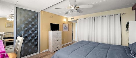Un dormitorio con cama, cómoda, ventilador de techo y ventana con cortinas.