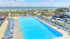 Ein Swimmingpool mit blauem Wasser, umgeben von Liegestühlen und Blick aufs Meer.