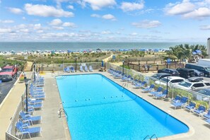 Ein Swimmingpool mit blauem Wasser, umgeben von Liegestühlen und Blick aufs Meer.
