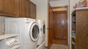 A laundry area with two front-loading washing machines, wooden cabinets, and a door leading to another room. - Ski In Ski Out Marvel with golf, biking, pool and fishing (Granby)