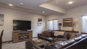 A living room with a leather couch, a flat-screen TV on a wooden cabinet, and a painting on the wall. - Ski In Ski Out Marvel with golf, biking, pool and fishing (Granby)