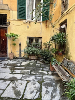 A courtyard with stone flooring, potted plants, a wooden bench, and a door. - Elegantly renovated apartment next to Aquarium & Waterfront (Genova)