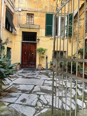 A courtyard with a stone pathway leading to a wooden door, surrounded by buildings with yellow walls and green shutters. - Elegantly renovated apartment next to Aquarium & Waterfront (Genova)