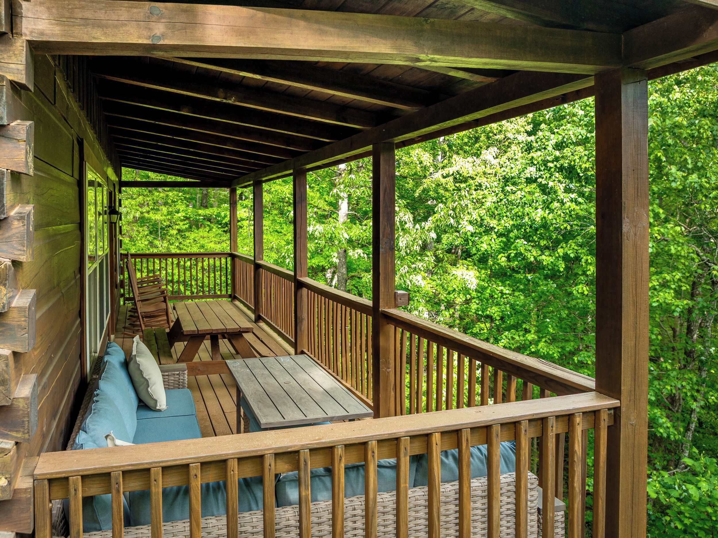 Eine Holzterrasse mit überdachtem Bereich, Korbmöbeln und Blick auf dichtes Grün.
