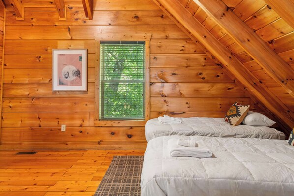 A wooden cabin room with two beds, a window with green blinds, a framed picture on the wall, and a wooden ceiling. - Cabin for 11 w/ Hot Tub, Game Room, Mountain Views (Gatlinburg)