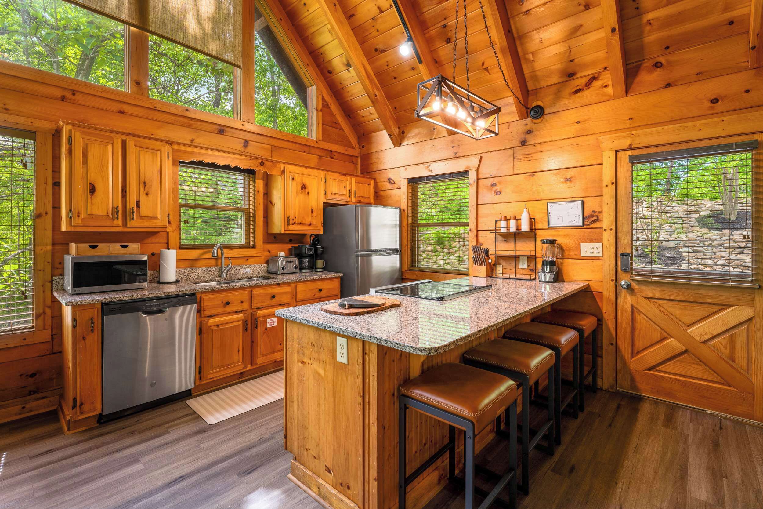 A wooden cabin kitchen with a central island, bar stools, and a large window.