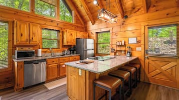 A wooden cabin kitchen with a central island, bar stools, and a large window.