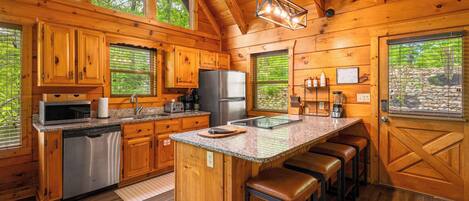 A wooden cabin kitchen with a central island, bar stools, and a large window.