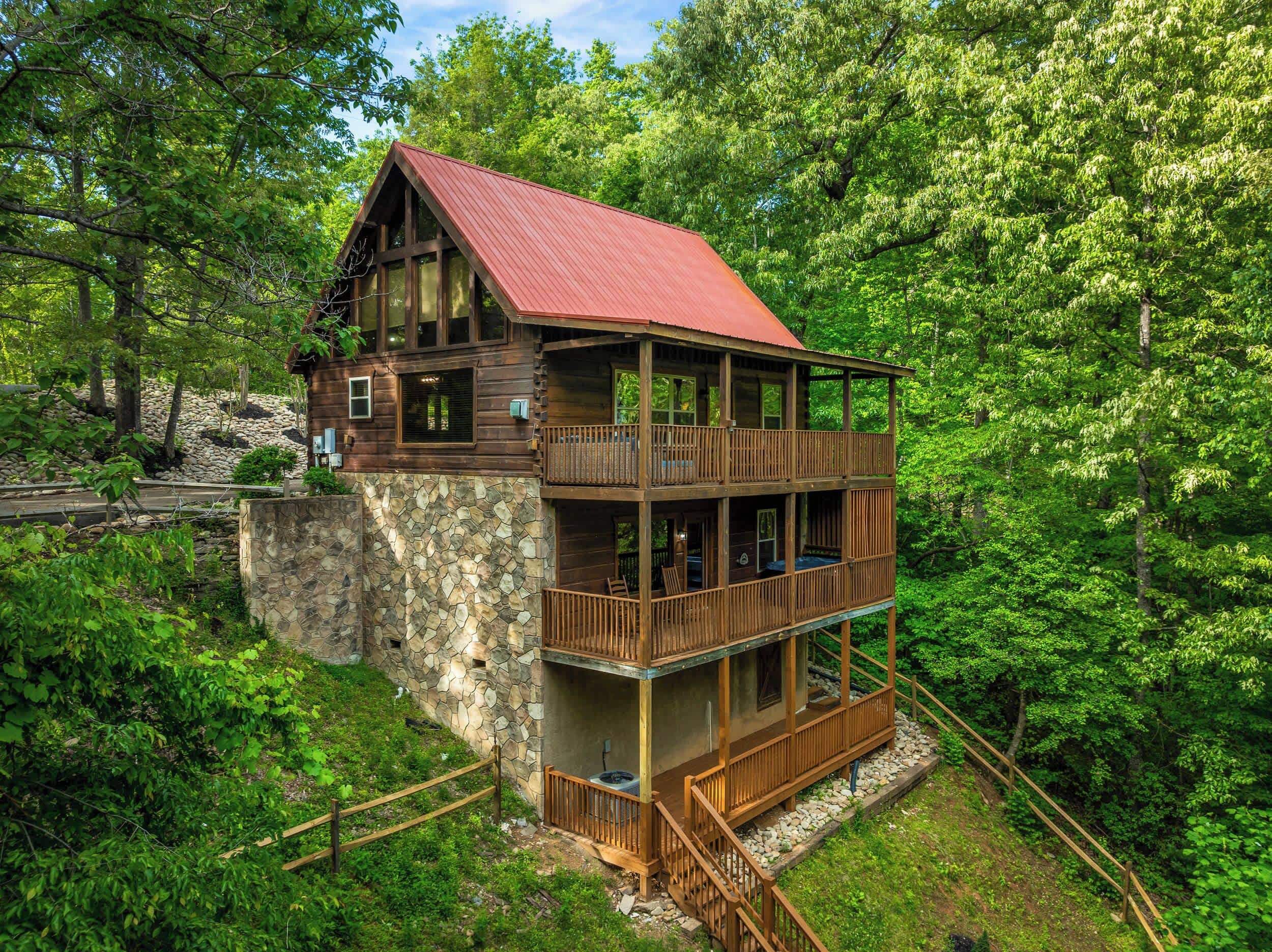 A multi-story wooden cabin with a stone foundation, surrounded by lush greenery.